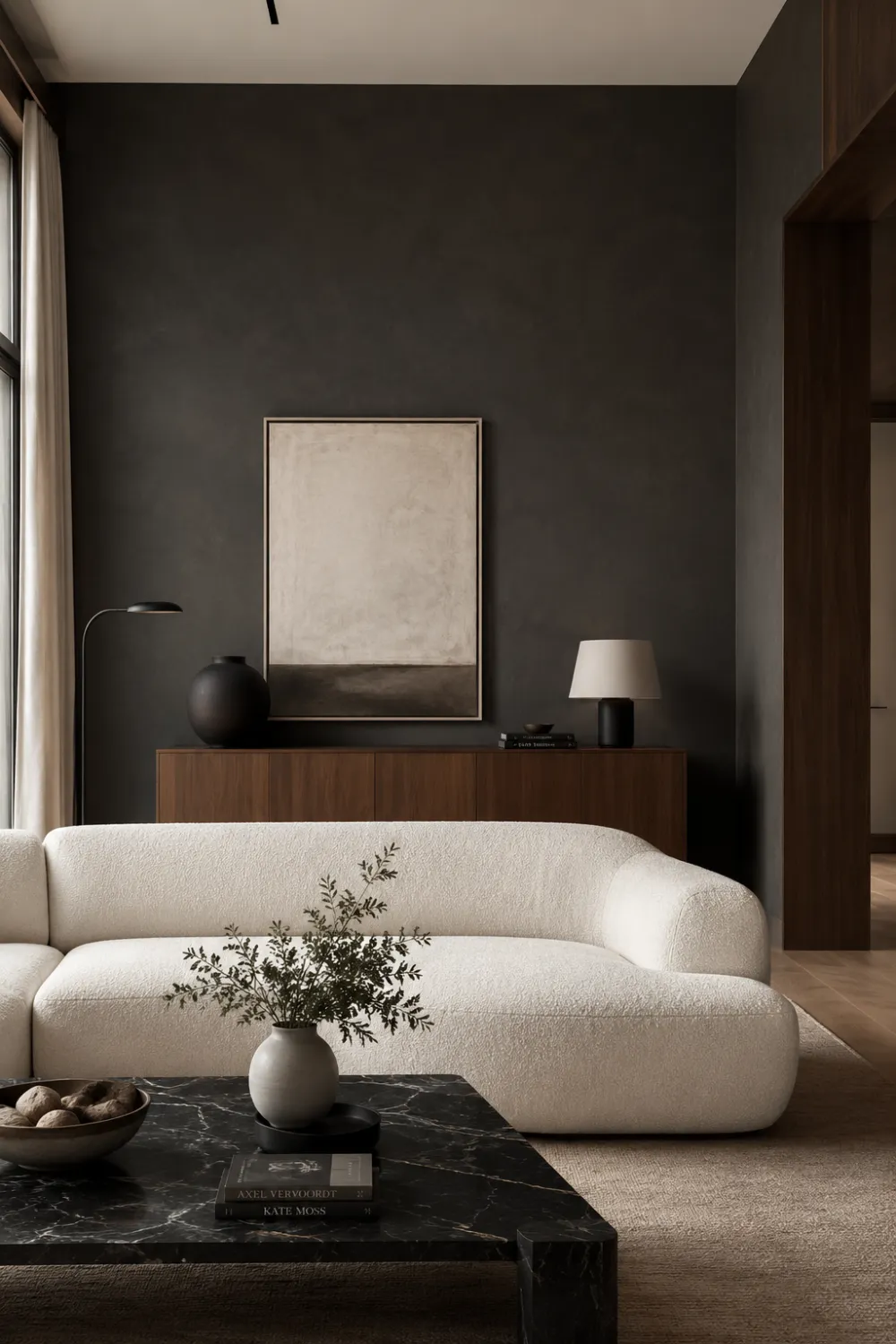Warm charcoal modern living room with cream curved sofa, black marble coffee table, dark textured walls, walnut wood cabinet, minimalist decor, and sophisticated quiet luxury interior styling with earthy modern tones.