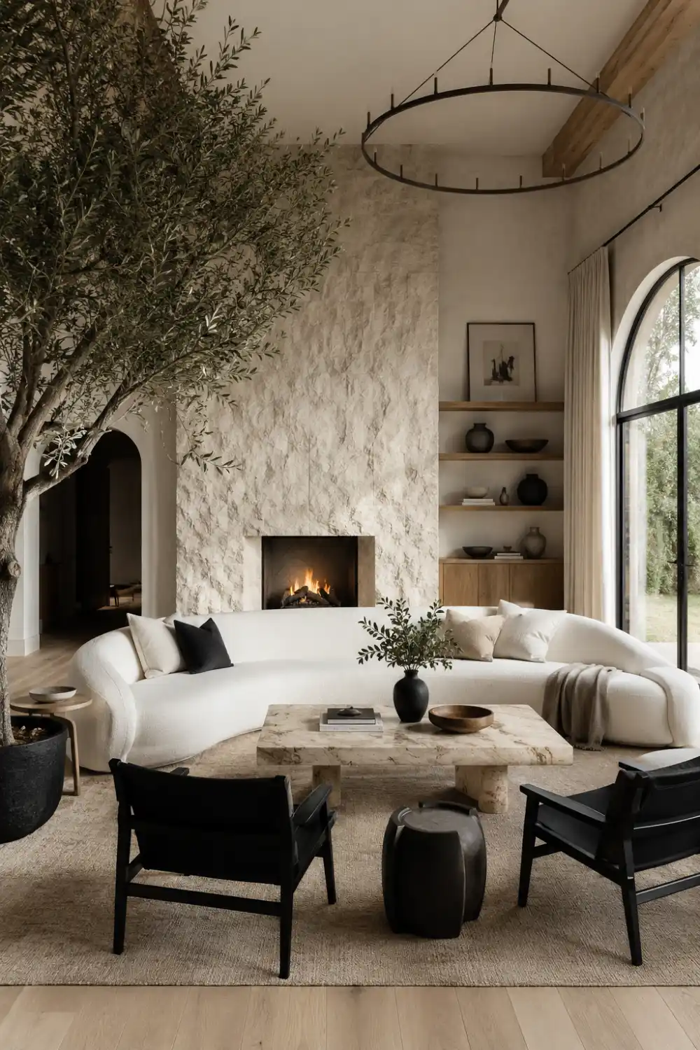 Organic modern black and white living room with curved sofa, stone fireplace, wood shelving, indoor tree, and natural textures.