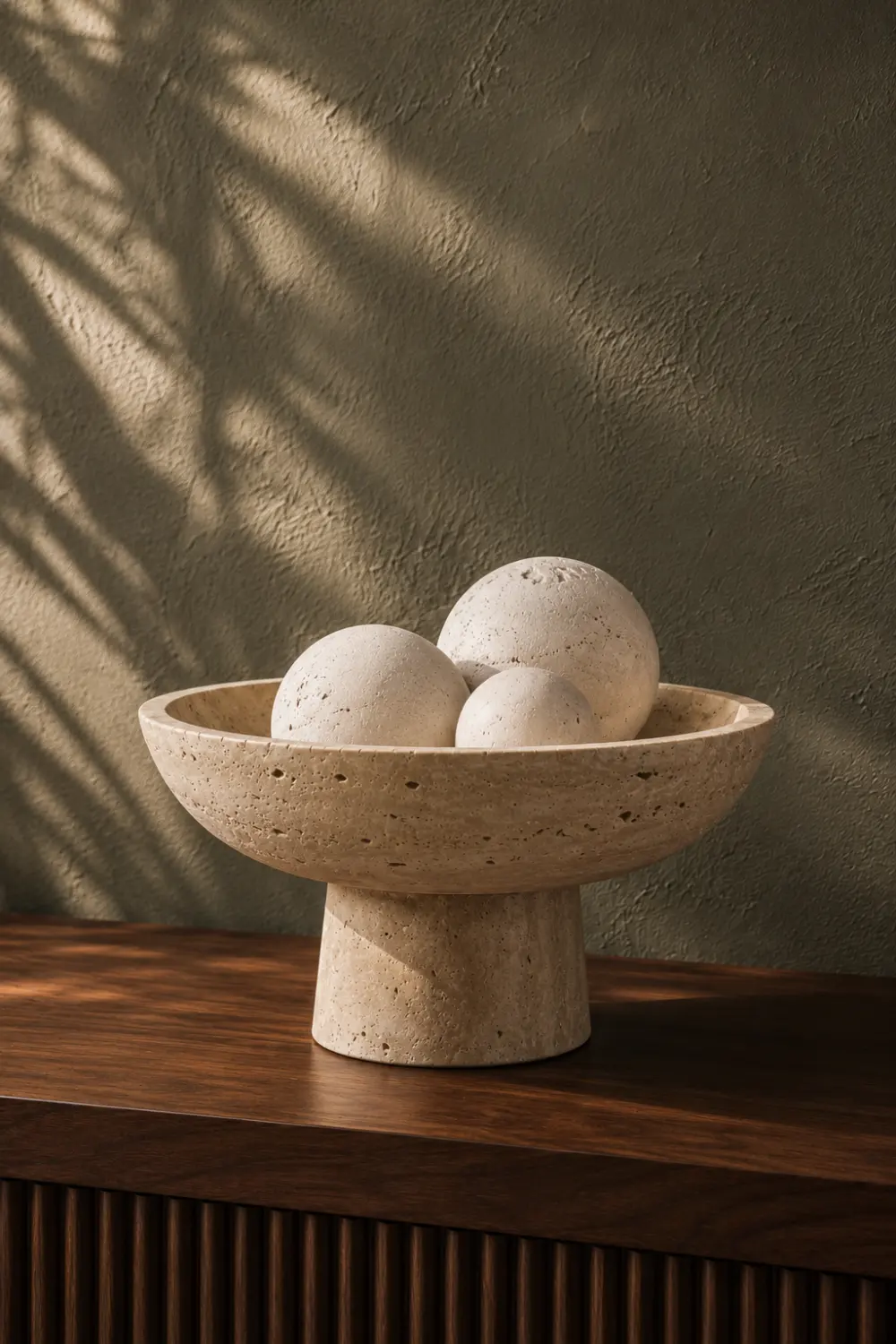 Travertine pedestal bowl with decorative stone spheres displayed on a walnut console table in a luxury modern home interior