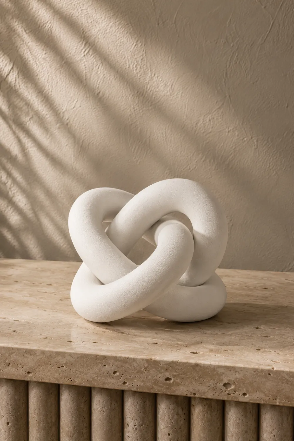 Modern white decorative knot sculpture displayed on a travertine console table in a contemporary luxury home with neutral decor styling