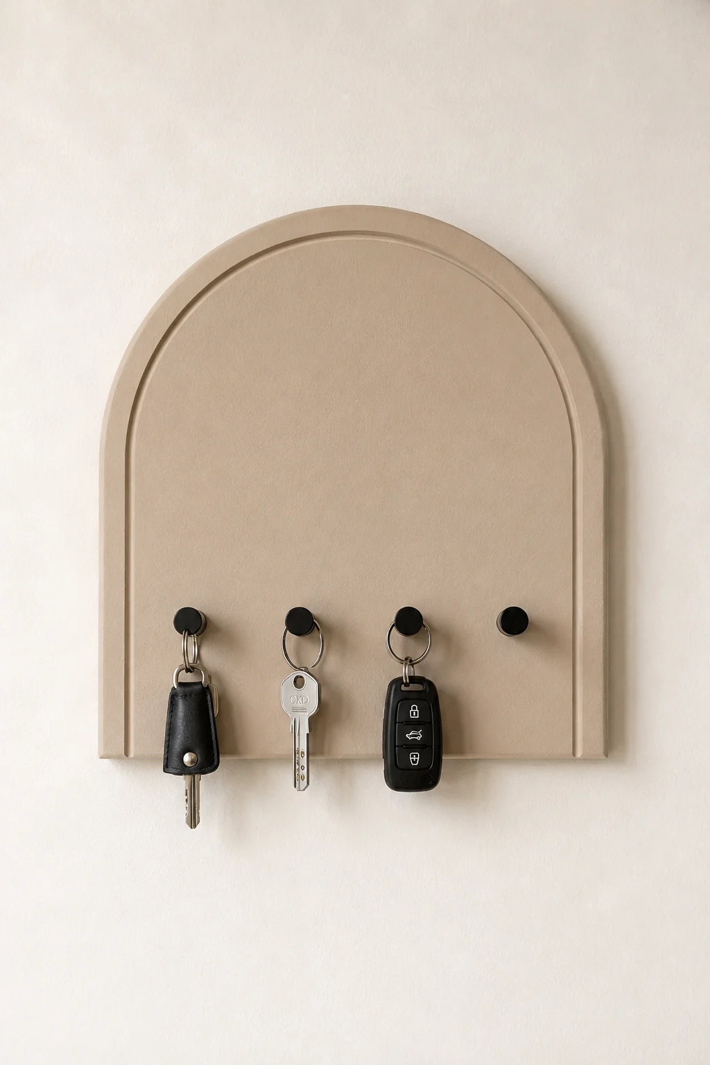 Modern arch shaped DIY key holder mounted on a soft neutral wall, featuring a warm beige finish, raised curved border, matte black hooks, leather keychain, house keys, and car keys for a stylish entryway wall organization idea.