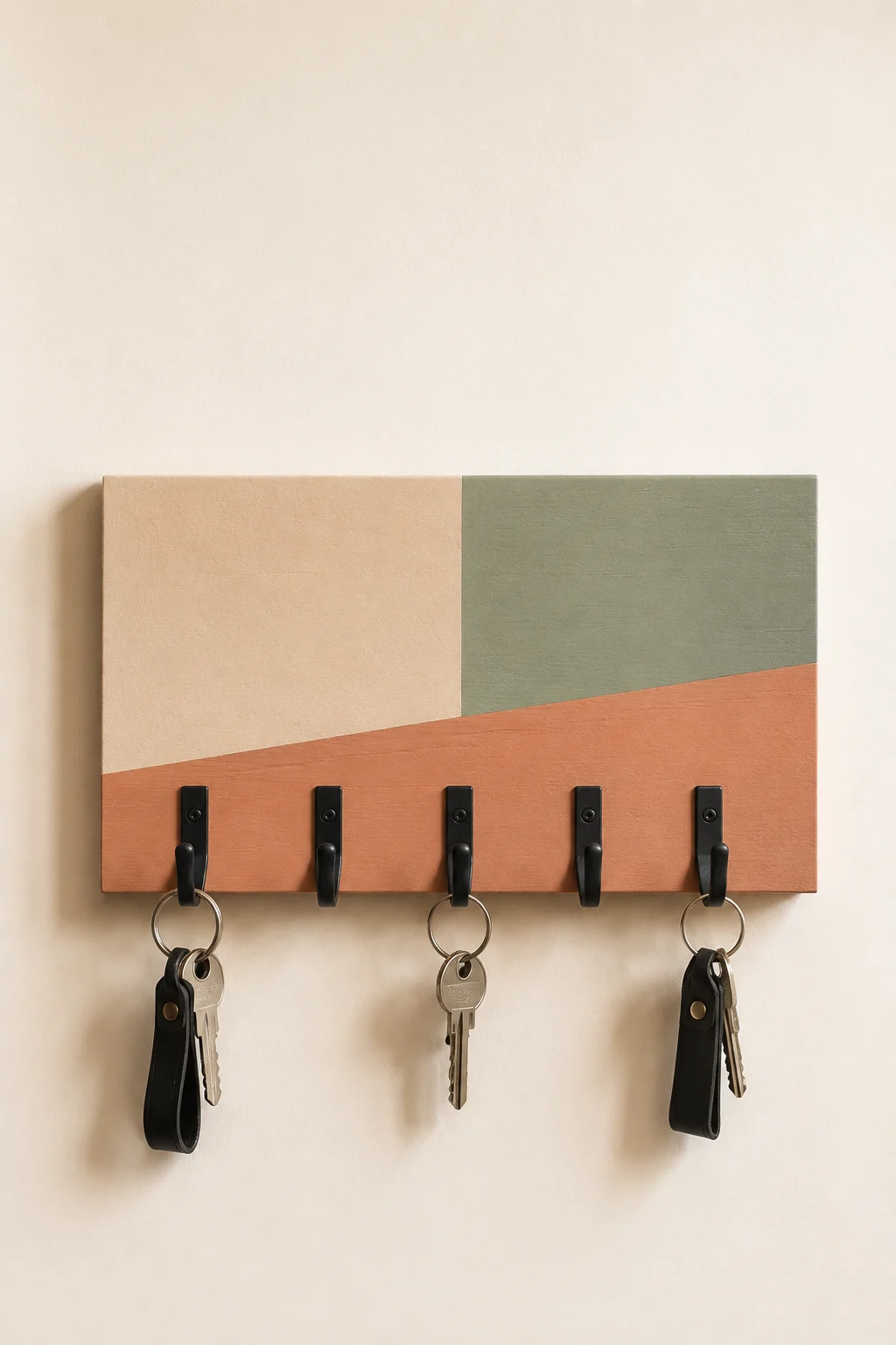 Modern color block DIY key holder featuring geometric sections in soft beige, muted sage green, and warm terracotta with matte black hooks, house keys, and leather keychains for colorful contemporary entryway organization.
