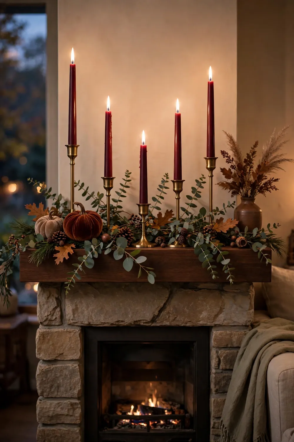 Fireplace mantel styled with deep burgundy taper candles in brass holders at varied heights with eucalyptus sprigs and fall foliage