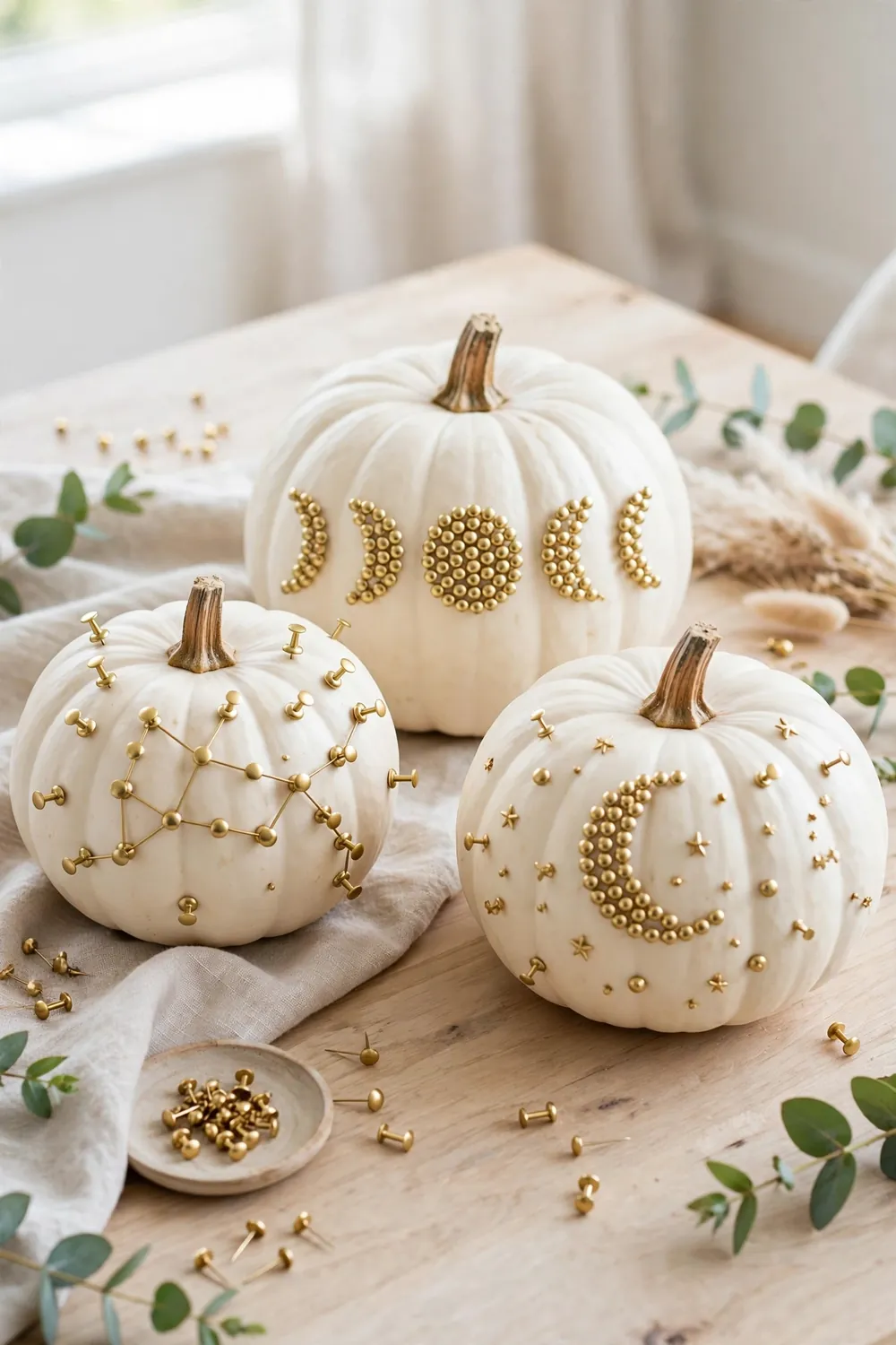 White pumpkins decorated with gold pushpin constellation patterns on a bright table